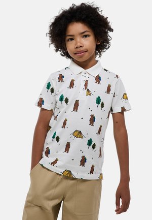 Polo shirt avec une base blanche présentant un motif de camping avec des ours, des arbres et des tentes dans des tons de marron, de vert et de jaune. Manches courtes et patte de boutonnage.
