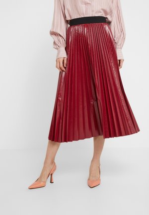 Roter plissierter Rock mit glänzender Oberfläche, schwarzem Taillenbund und mittellanger Länge, kombiniert mit pfirsichfarbenen High Heels.