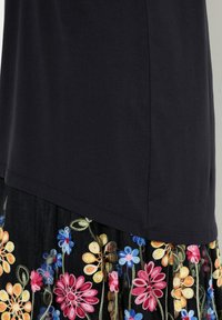 Top negro de tela suave con dobladillo curvado, superpuesto a una falda bordada con flores que presenta coloridas flores sobre una base negra transparente.