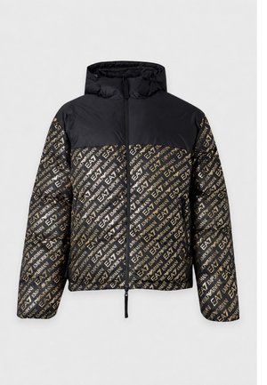 Homme portant une doudoune noire et dorée à motifs, une chemise noire, un pantalon beige et des chaussures noires, debout devant un fond blanc uni.