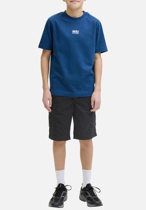 Garçon portant un t-shirt bleu Jack & Jones, un short cargo noir, des chaussettes blanches et des baskets noires, debout les bras détendus le long du corps.