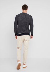 Maglione a maglia blu navy con polsini e orlo a coste, abbinato a pantaloni chinos beige e sneakers bianche con suola marrone.