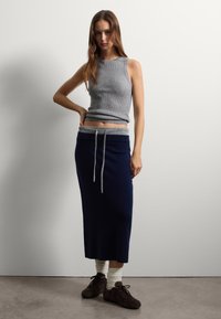 Top in cotone grigio a coste e gonna lunga blu navy con cintura grigia regolabile. Abbinati a sneakers marroni e calzini bianchi a coste. Texture lisce.
