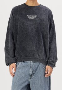 Tummanharmaa collegepaita, jossa ovat lasketut olkapäät, resorit hihansuissa ja helmassa. Edessä valkoinen teksti "MOONLIGHT ROMANCE". Pehmeä, teksturoitu kangas.