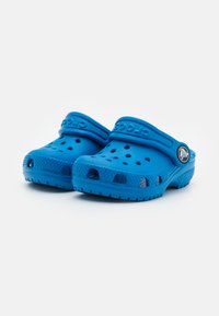 Zilā krāsa Crocs klogi, kas izgatavoti no viegla materiāla, ar ventilācijas caurumiem, izliektu dizainu un aizmugurējo siksniņu drošai piegulšanai.