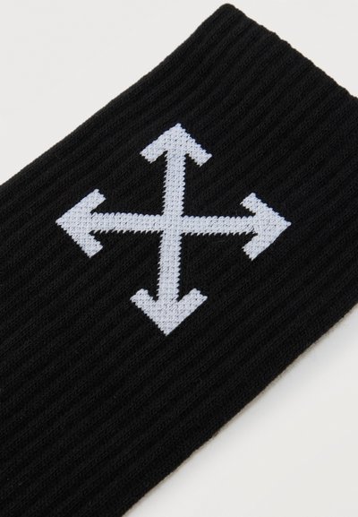 Tissu noir tricoté avec un symbole de flèche en forme de croix blanche pointant vers le haut, le bas, la gauche et la droite sur un fond uni.