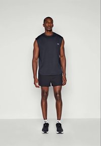 Black sleeveless athletic top paired with black shorts. Features a rounded neckline and smooth fabric, complemented by black athletic shoes.