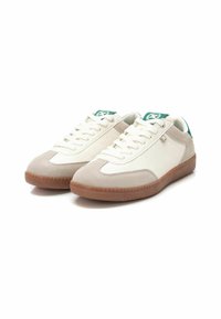 Zapatillas blancas y grises con parte superior de ante y cuero, que cuentan con una suela de goma texturizada y detalles verdes en el talón y la lengüeta.