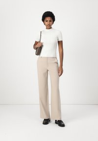 White ribbed short-sleeve top paired with beige wide-leg trousers. The outfit is complemented by black shoes and a small handbag.