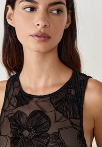 Schwarzes, transparentes Oberteil mit floraler Stickerei, ärmellosem Design und rundem Ausschnitt, ausgestattet mit einer glatten Textur und detailliertem Stoffmuster.