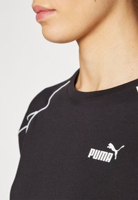 Melnā T-kreklā ar baltu Puma logo, īsām piedurknēm un piegulstošu apkakli. Piedāvā kontrastējošu baltu šuvumu plecu šuvē.