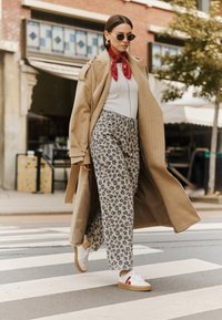 Beige pinstriped coat over a white top, paired with light brown and gray leopard print pants. White sneakers with red accents. Sunglasses worn.