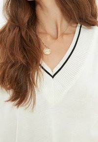 Sweter w kształcie litery V w kolorze białym z czarnymi akcentami, wykonany z materiału typu ribbed knit. Charakteryzuje się luźnym krojem i gładką teksturą. Złoty okrągły naszyjnik.