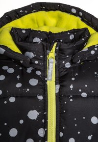Černá bunda s šedými skvrnitými vzory, žlutou fleecovou podšívkou a jasně žlutým zipem. Má vysoký límec a prošívaný design.