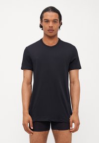 T-shirt noir à manches courtes en tissu doux, avec un col rond, une coupe décontractée et une texture lisse. Sans motifs ni accents visibles.