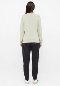 Hellgr�ünes Sweatshirt mit gerippten Ärmelbündchen und Saum, kombiniert mit einer dunklen, lässig geschnittenen Hose. Das Model trägt weiße Sneakers mit schwarzen Akzenten.