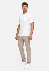 Witte katoenen t-shirt met korte mouwen en een borstzak, gecombineerd met beige broek en witte sneakers. Eenvoudig, schoon ontwerp met subtiele accenten.