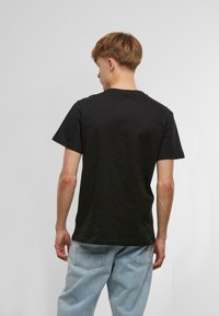 Black cotton t-shirt with a crew neckline, short sleeves, and a relaxed fit, paired with light blue jeans featuring back pockets.