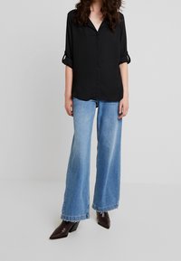 Black, short-sleeved shirt with a V-neck and rolled sleeves, paired with light blue wide-leg jeans and dark pointed-toe heeled boots.