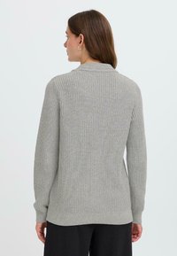 Pull en tricot gris clair avec une texture côtelée, doté de manches longues et d'un col arrondi. L'ourlet est légèrement plus long à l'arrière.