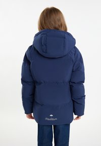 Giacca imbottita blu navy con cappuccio, caratterizzata da una texture liscia e polsini elasticizzati. Dettaglio del logo vicino all'orlo, abbinata a jeans in denim.