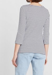 Randig långärmad topp i marinblått och vitt, med rundad halsringning och avslappnad passform, bärs tillsammans med ljusblå högmidjade jeans.