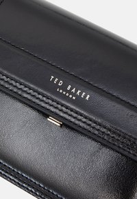 Czarna skórzana portmonetka o teksturowej powierzchni i wytłoczonym logo marki, z zapięciem w kolorze złotym i szczegółowym przeszyciem wzdłuż krawędzi.