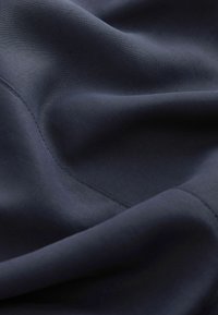 Tissu bleu foncé avec des coutures visibles et des plis doux, mettant en valeur une texture lisse et un tissage fin détaillé.