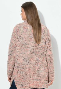 Stickad cardigan i beige garn med röda och lila inslag. Lätt lös passform, sidofickor och långa ärmar. Texturen verkar mjuk och mysig.