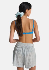 Bralette bleu avec bretelles réglables, associée à un short bleu clair à rayures verticales, doté de poches et d'une ceinture élastique.