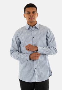 Camisa abotonada de color azul claro con un pequeño patrón geométrico, de mangas largas y un cuello clásico. Hecha de una tela suave, adecuada para un uso casual.