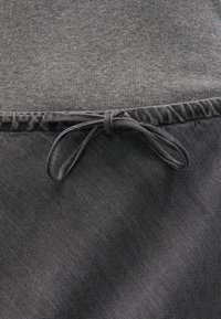 Prenda gris con una superficie texturada. Presenta un cordón ajustable a la altura de la cintura, con un acabado suave y un sutil patrón acanalado.