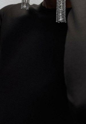 Persona que lleva una blusa negra y largos pendientes plateados colgantes con varias filas de pequeñas cuentas o cristales.