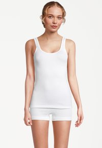 Canotta bianca con spalline larghe e scollo arrotondato, abbinata a pantaloncini bianchi. Entrambi sono realizzati in tessuto di cotone liscio e aderente.