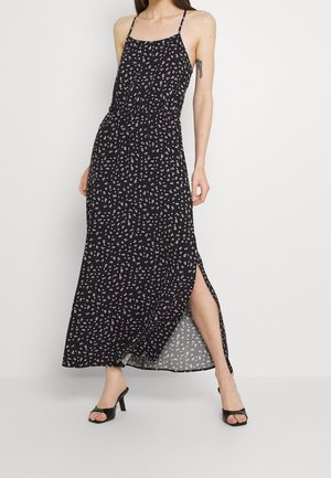 Czarna maksymalna sukienka w kwiatowy wzór, z regulowanymi ramiączkami, elastyczną talią i bocznym rozcięciem. Noszona z czarnymi sandałami na wysokim obcasie.