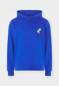 Blå hoodie gjord av mjukt tyg med en framficka, dragsko i huvan och en fyrkantig logotyp med en leende ansikte.