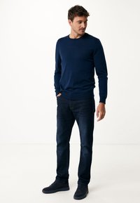 marineblauer gestrickter Pullover mit Rundhalsausschnitt, taillierten Bündchen und Saum, kombiniert mit dunklen Jeans und blauen Wildledersneakern.