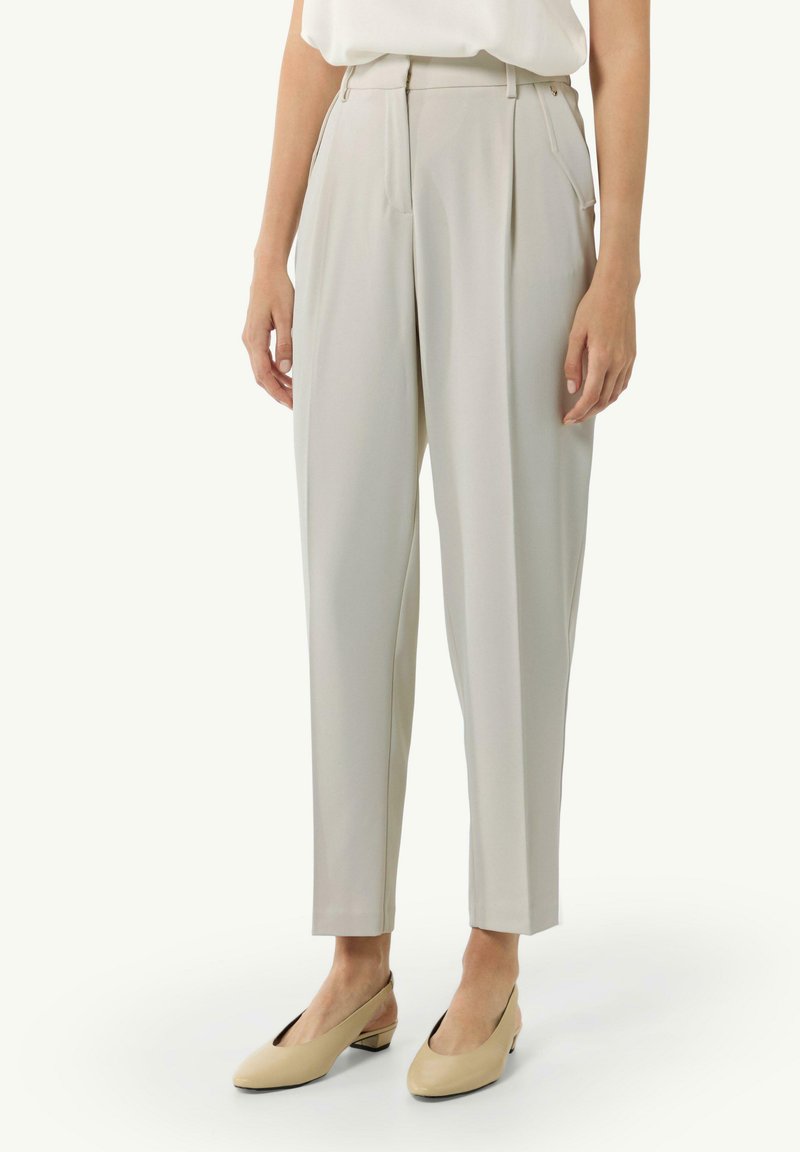 Jasnoszare spodnie z wysokim stanem, z zakładkami i gładką fakturą, z bocznymi kieszeniami i zwężającymi się nogawkami. Połączone z beżowymi butami na obcasie typu slingback.