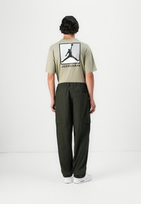 Kaki T-shirt med et stort sort Jordan-logo på ryggen, sammen med olivengrønne cargo-bukser med sidelommer og elastisk talje.