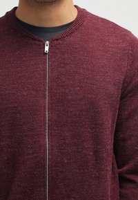 Burgundowa sweter na zamek z okrągłym dekoltem, wykonany z teksturowanej dzianiny. Ma srebrny zamek z przodu i ściągacze przy mankietach.
