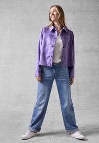Veste courte violette avec un devant à boutons et deux poches poitrine, assortie à un jean bleu clair ample et des baskets blanches.