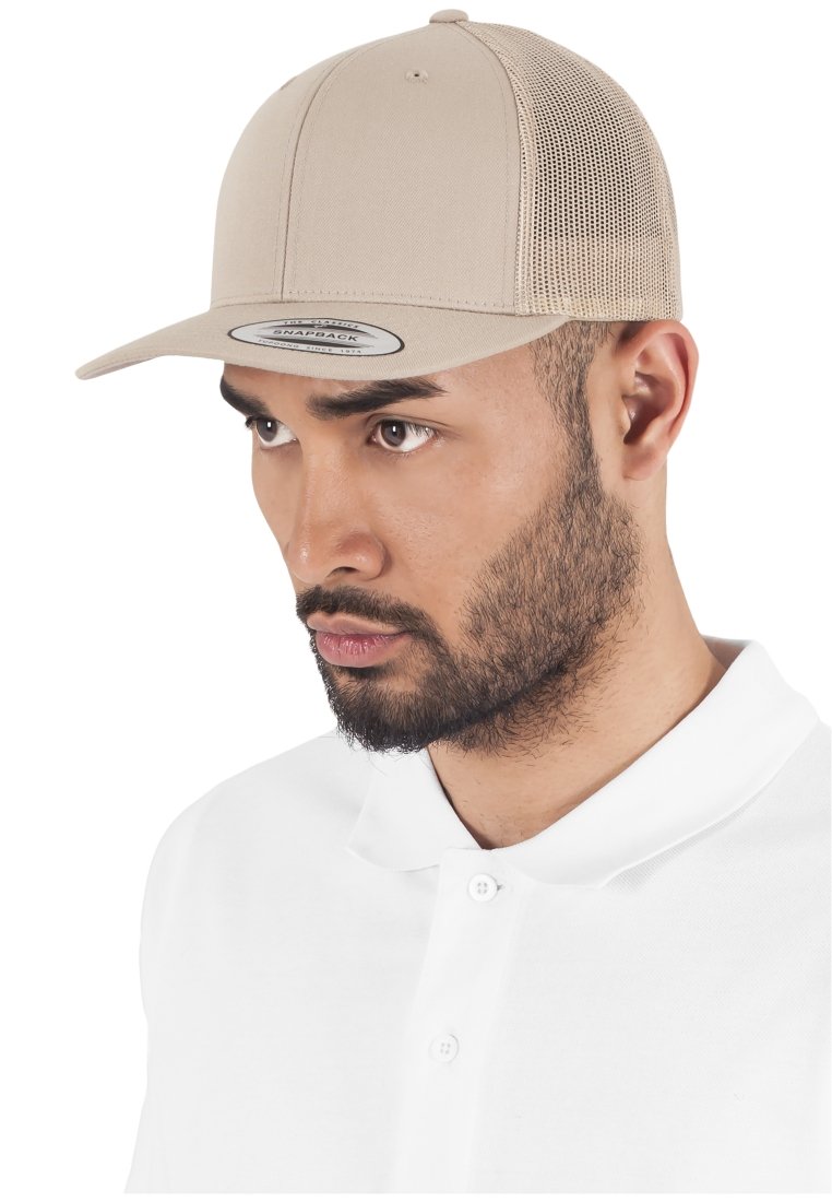 Cappello snapback beige con parte frontale rigida, retro in rete per ventilazione e un'etichetta ovale sulla visiera. Indossato da una persona con una polo bianca.