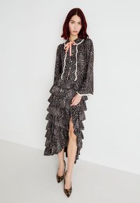 Svart og beige leopardmønstret kjole med volanger, lange ermer, hette og en rosa sløyfedetalj ved halsen. Høy splitt på venstre side.