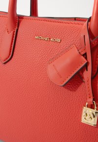 Punane kivi tekstuuriga nahk käekott kuldse "MICHAEL KORS" logoga, siledate aktsentidega ja nahk sildiga. Omab kaht kät ja metallist võtmehoidjat.