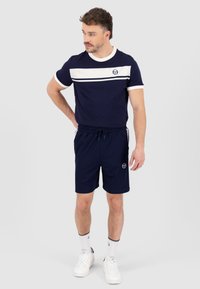 Marineblå T-skjorte med hvite horisontale striper, rund hals, sammen med marineblå shorts med elastisk midje og logo-detalj. Hvit sneakers.