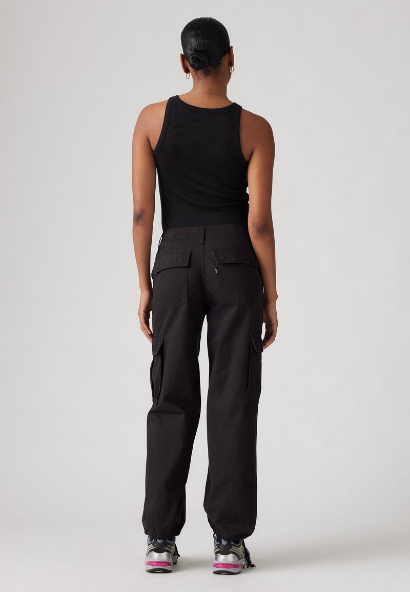 Pantalons cargo noirs avec plusieurs poches, une coupe décontractée et des poignets élastiques. Assortis à un débardeur noir ajusté et des chaussures de sport.