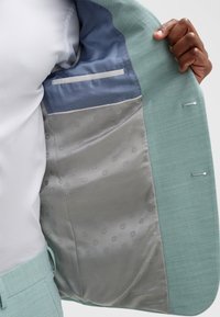 Mint green suit jacket interior featuring a light blue lining and a flower pattern on a gray fabric. Includes one pocket and a smooth texture.