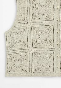 Krämfärgad virkad väst med fyrkantiga blommönster, knappstängning på högra sidan och öppet spetssmide.