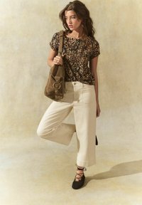 Top a maniche corte con stampa leopardata, pantaloni ampi crema e scarpe nere con lacci. Borsa a spalla marrone con dettaglio circolare in metallo.