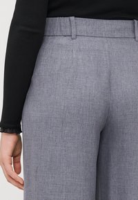 Grijze op maat gemaakte broek van een zachte, gestructureerde stof, met een aansluitende tailleband en zijzakken. Het ontwerp heeft een lichte glans.